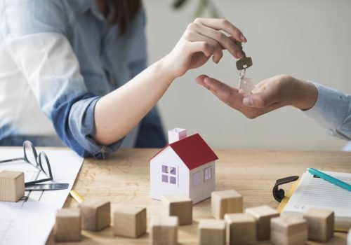 close-up-woman-s-hand-giving-house-key-man-wooden-table
